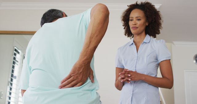 Biracial female physiotherapist talking to senior man holding his back - Download Free Stock Photos Pikwizard.com