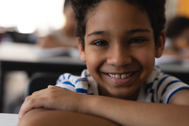 Close-up of happy school boy leaning on desk and looking at camera in classroom of elementary school