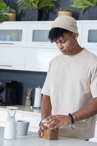 Young man opening jar of brown sugar in modern minimalist kitchen with plants