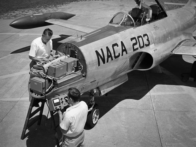 The image depicts two technicians installing an audio recording machine and sensors on a Lockheed F-94B Starfire at the NACA Lewis Flight Propulsion Laboratory. This scene captures a moment in aerospace history, illustrating the technical efforts to study and mitigate noise caused by jet engines as airline manufacturers prepared to introduce them in passenger aircraft. This image is suitable for use in articles, presentations, and educational content about the history of aviation, noise control research, and aerospace engineering advancements.