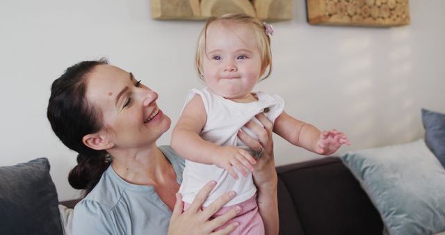 Caucasian mother smiling while holding her baby sitting on the couch at home. motherhood, love and childcare concept