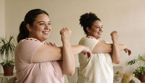 Curvy friends stretching shoulders in living room practicing gentle home workout together