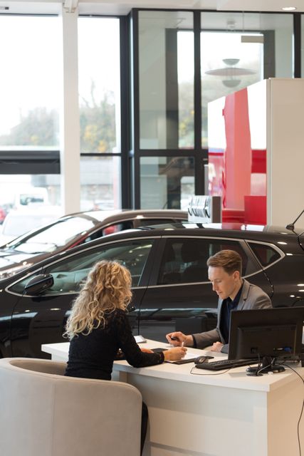 Female customer discussing with salesman while sitting at desk in carshowroom
