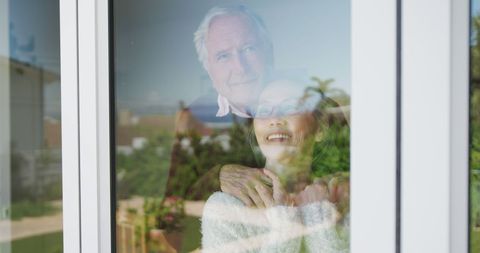 Happy Senior Couple Embracing While Looking Through Window