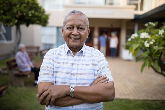 Portrait of smiling senior man standing with arms crossed against retirement home