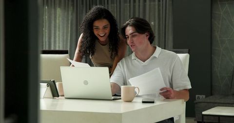 Couple Reviewing Documents Together at Home with Laptop and Coffee