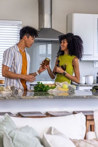 Multiracial couple unpacking groceries at modern kitchen island with reusable bags