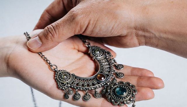 Hands exchanging ornate crescent pendant with blue-green cabochon and filigree details