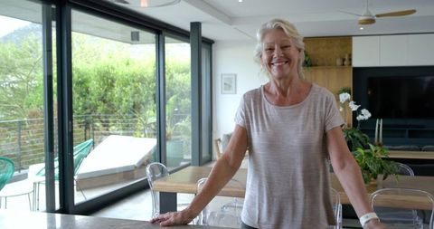 Smiling senior woman leaning on kitchen island wearing smartwatch in modern open-plan home