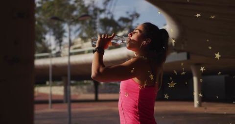 Woman drinking water during urban workout pause under pavilion backlit by golden sunlight
