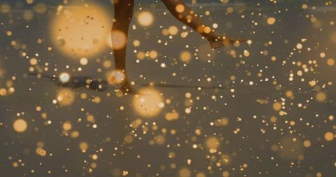 Barefoot walking across reflective studio floor with golden bokeh orbs and glowing motion