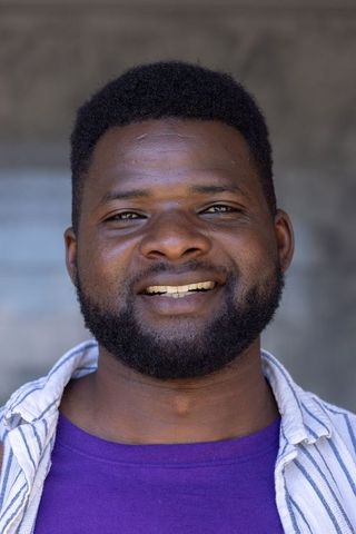 Smiling man wearing purple crewneck and striped open shirt, friendly portrait headshot