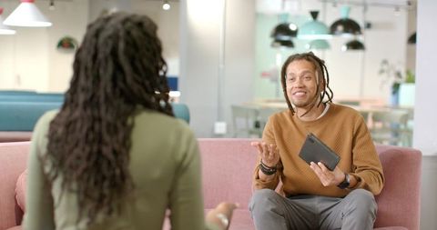African American Coworkers Discussing Project on Pink Sofa in Modern Open-Plan Office