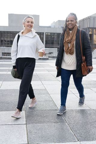 Senior diverse women walking together in urban plaza enjoying coffee and conversation