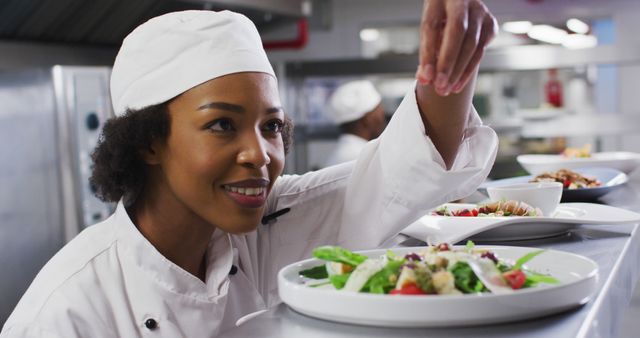 Female chef garnishing a gourmet dish in a bustling restaurant kitchen. Suitable for food industry promotions, culinary arts education materials, chef training resources, restaurant marketing content, and hospitality industry advertisements.