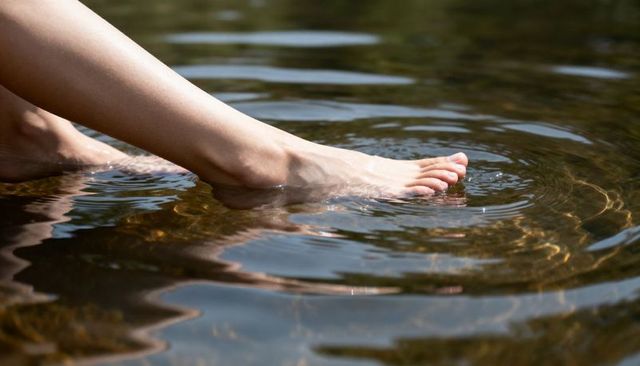Dipping Bare Feet in Shallow Clear Water with Sunlit Ripples and Pebble Reflections