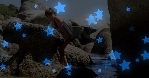 Child climbing granite boulders by clear tidal pool on summer day
