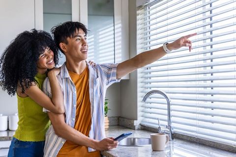 African american woman and asian man admiring sunlight through blinds in modern kitchen