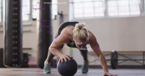 Mid-adult woman balancing one-handed plank on medicine ball in gym, building core strength