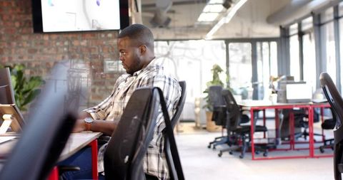 Typing man concentrating on laptop in modern open-plan office with industrial design