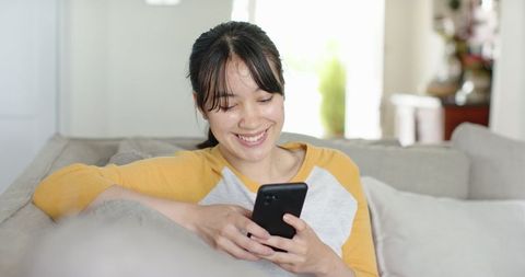 Asian Woman Relaxing Indoors Using Smartphone