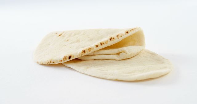 Two pieces of pita bread are displayed against a white background, with copy space. Pita bread is a staple in many Middle Eastern and Mediterranean cuisines, often used to scoop sauces or fill with various ingredients.