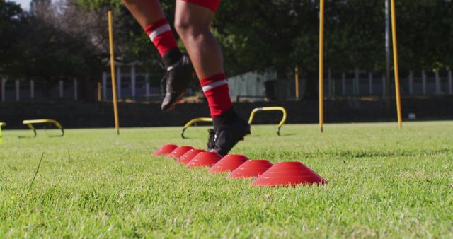 Athlete conducts agility drills with cones on a grassy field. This image is ideal for use in sports or fitness training articles, promoting outdoor exercise, or advertising athletic gear. The grassy setting and bright colors emphasize an active and healthy lifestyle.