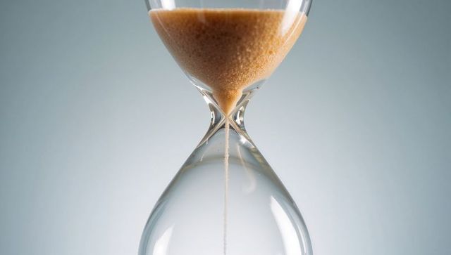 Elegant hourglass with flowing fine sand on grey background