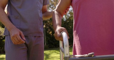 Male caregiver assisting senior woman with walker outdoors