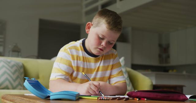 Young boy concentrating on doing his homework at a table in a comfortable living room. Can be used for educational, parenting, and remote learning concepts. Suitable for illustrating the importance of home study environments for children.