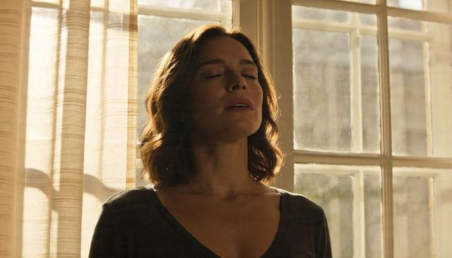 Woman standing by sunlit window breathing deeply, serene contemplative calm warm rimlight