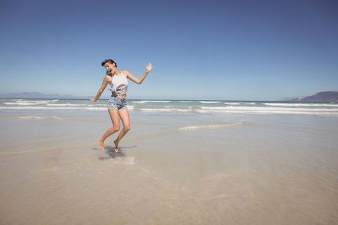 Joyful woman jumping on pristine beach under blue sky