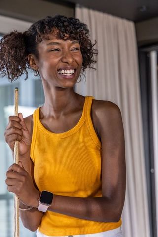 Laughing woman holding pool cue wearing mustard tank top and pink smartwatch