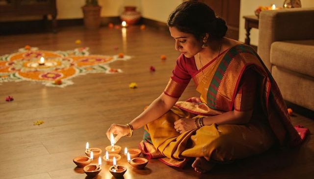 Lighting diyas for diwali by indian woman in mustard silk sari with rangoli