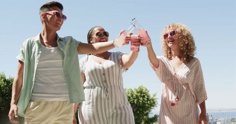 Joyful celebration friends toasting refreshing drinks outdoors in sunshine