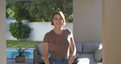 Confident african american woman standing on modern patio by pool wearing brown tee