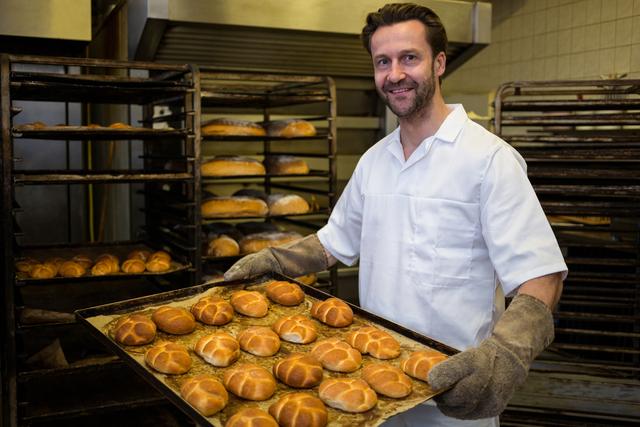 Smiling baker carrying a tray of baked buns - Download Free Stock Photos Pikwizard.com