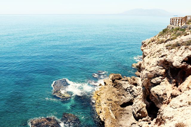 Image captures stunning ocean view with clear blue water and waves crashing against rocky cliffs on sunny day. Ideal for travel websites, vacation brochures, nature blogs, or outdoor adventure promotions.