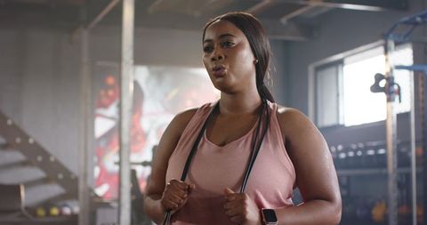 African american woman pausing during workout holding jump rope in sunlit industrial gym