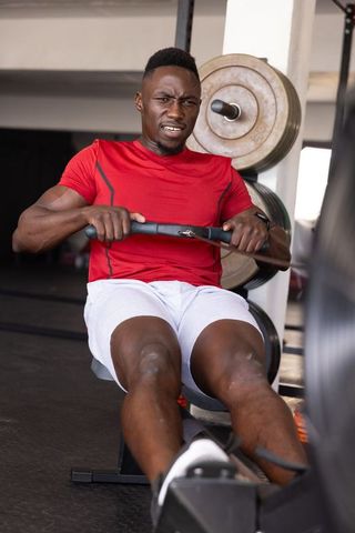 African american man pulling rowing machine during intense gym workout