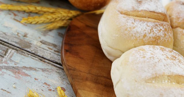 Freshly baked bread rolls on a wooden board with wheat stalks highlight the natural ingredients and homemade charm. Perfect for use in food blogs, bakery advertisements, kitchen decor inspiration, or recipes emphasizing natural and fresh ingredients.