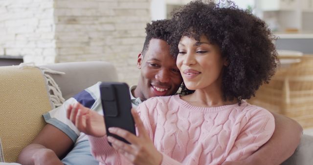 Happy african american couple using smartphone together in living room. Spending quality time at home together concept.
