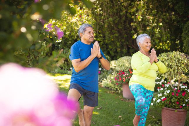 Biracial senior couple looking away while exercising in prayer position against plants at park. nature, unaltered, yoga, love, togetherness, retirement, fitness and active lifestyle concept.