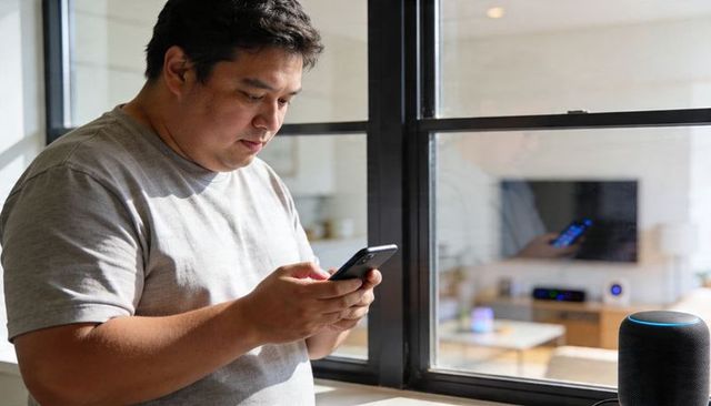 Asian man using smartphone by window with smart speaker minimalist home tech lifestyle