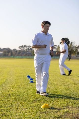 Cricket teammates jogging through agility cones on grass field wearing white kit