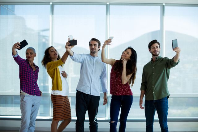 Creative business team taking selfie with mobile phone in office