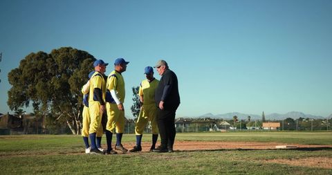 Baseball team huddling with coach on infield in yellow uniforms, teamwork and leadership
