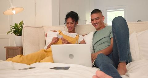 Couple enjoying online shopping together on cozy bedroom bed