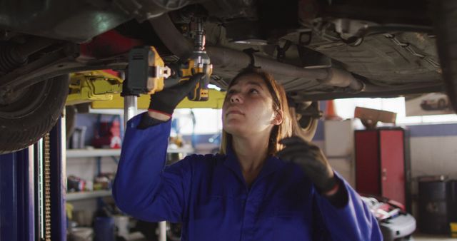 Female mechanic using a power drill and working under a car at a car service station. automobile repair service