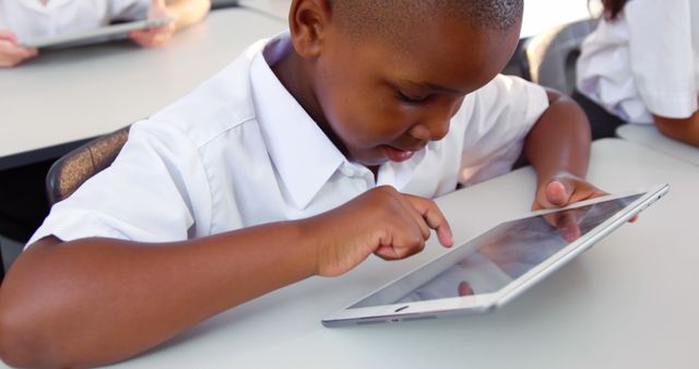 Young African American boy engaged with tablet during class time. Ideal for illustrating modern education, use of technology in schools, e-learning, digital learning resources, and student activities in educational settings.